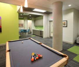 Game room with billiards table, green accent wall, and kitchenette in the background