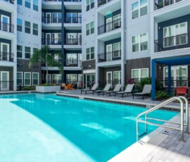 Resort-style pool with lounge chairs and blue pergola at Legacy ENCORE! Luxury Apartments