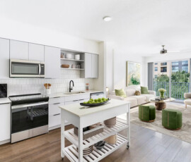 Modern apartment kitchen and living area with white cabinetry, black stove and range, white subway tile backsplash, island with storage, beige sofa in adjacent living room, green accent poufs, balcony doors.